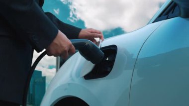 Elektrikli araç, iş adamı yüksek gökdelenlerle çevrili kentsel alandaki şarj istasyonunda EV akü şarj ediyor. Çevre dostu yenilikçi temiz enerji kavramı.