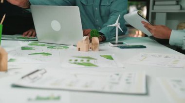 Bir grup profesyonel, yeşil enerji kavramları ve büyüme grafikleriyle çevrili bir ofis ortamında işbirliği yaparak, sürdürülebilirlik ve strateji planlamasında takım çalışmasını vurguluyor. SACTR