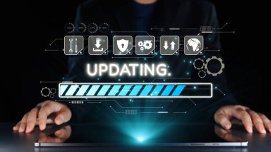 Bir iş adamı, sistem güncellemelerini izlerken dizüstü bilgisayarla etkileşime girer, teknolojinin gelişimini sembolize eden parlak bir ilerleme çubuğu ve dijital arayüz unsurlarını gösterir. Dörtgen