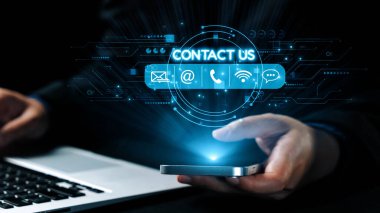 Bir iş adamı iletişim bilgilerine erişirken akıllı telefonla iletişim kurar. Dijital simgeler cihazın etrafını sarar, profesyonel ortamdaki modern iletişim yöntemlerini sembolize ederler. Dörtgen