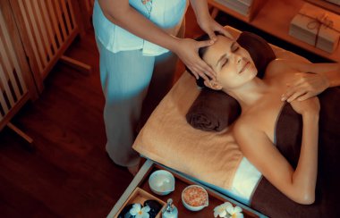 Beyaz kadın stres önleyici kafa masajı yapmaktan ve lüks otel veya otelde sıcak mum ışığında yüz güzelliği eğlencesi yapmaktan zevk alıyor. Sessiz.