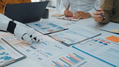 İnsanlar analiz ve strateji tartışmalarında yer alırken, robot bir elin finansal raporlar ve çizelgelerle etkileşime girdiği ortak bir çalışma alanı sahnesi.