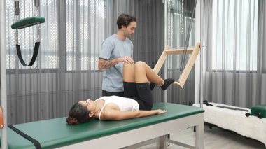 Pilates hocası, Cadillac teçhizatı üzerindeki bacak kaldırma egzersizi sırasında bir müşteriye yardım ediyor. Öğrenci uzanıyor ve temel dayanıklılık ve bacak esnekliğini arttırmak için Cadillac 'ın üzerinde bacak daire çiziyor. Alışkanlık.