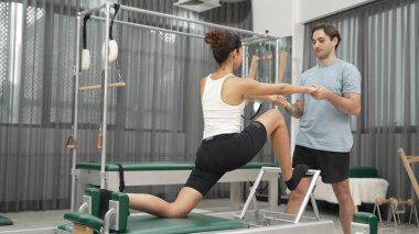 Esneklik ve çekirdek eğitimi için pilates kursunda trapez masasında destek alan bir kadın. Öğrenci dengeyi geliştirmek için reformcuları iki büklüm ediyor. Alışkanlık.