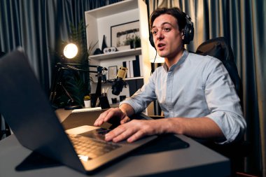 Sunucu kanalı akıllı yayıncı laptopta canlı sosyal medya uygulaması arıyor, kulaklık takıyor ve modern ofis stüdyosundaki mikrofonu kullanıyor. Bireysel.