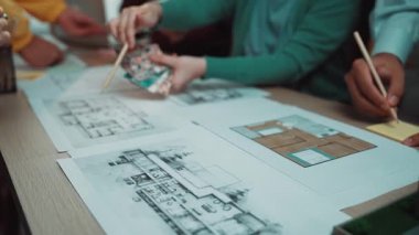 Çeşitli bir ekip, modern ofis ortamında taslak ve planları incelerken mimari tasarım ve kavramları tartışan ortak bir toplantıya katılıyor. SACTR
