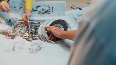 Mühendisler modern bir atölyede bir motorun ayrıntılı planları üzerinde işbirliği yaparak, takım çalışması ve tasarım ve yenilik süreçlerinde teknik uzmanlığı vurguluyorlar. SACTR