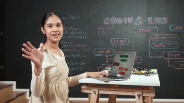 Akıllı liseli kız karatahtaya kod yazarken ya da daktilo yazarken kameraya el sallıyor. Dizüstü bilgisayar ya da yazım programı ve selamlama üzerine çalışan akademik öğrenci. Öğretim