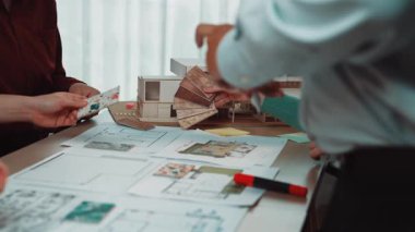 Bir grup profesyonel modern bir çalışma alanında iç tasarım fikirlerini tartışıyor. Yenilikçi bir proje üzerinde çalışırken planlar, renk örnekleri ve çizimler gözden geçiriyorlar. SACTR