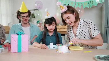 Kafkasyalı anne doğum günü pastasını kesiyor ve babaya verirken tatlıyı ayırıyor. Mutlu aile, kızının doğum gününde masada otururken parti şapkası takar. Özel durum konsepti. Pedagoji.