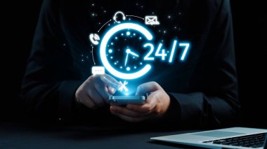 Bir kişi, modern bir iş bağlamında iletişim ve destek için 24 saatlik kullanılabilirliği sembolize eden dijital bir saat sergileyen bir akıllı telefondan yararlanıyor. Dörtgen