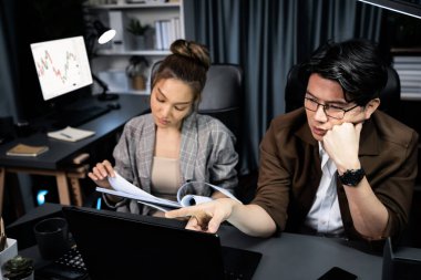 Stresli suratlı iki yönetici birlikte evrak işlerini tartışıyorlar. Modern ofiste gece geç saatlerde dizüstü bilgisayarla karşılaştırıldığında şirket projesinde çalışıyorlar. İnfobahn.