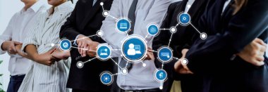 Profesyonel bir takım iş kıyafetleri içinde, dijital bağlantı ikonları ile geliştirilmiş, modern takım çalışması dinamiği ve birliği yansıtan işbirliği ve ağı sembolize ediyor. Dostluk
