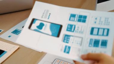 Mobil uygulama için kullanıcı arayüzü prototipini ofis çalışanlarına sunan harika bir şirket çalışanı. UX UI tasarımcısı kağıt üzerinde simge tasarımının işlevini açıklıyor. Sinerjik