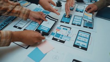 Çeşitli bir ekip, modern bir çalışma masasındaki kablo çerçevelerini ve prototipleri inceleyerek, yaratıcılığı ve yeniliği teşvik ederek, işbirlikçi mobil uygulama tasarımına girişir. SACTR