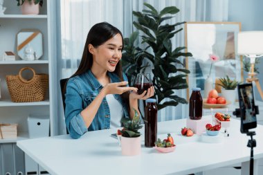 Gülümseyen, güzel Asyalı genç, lezzetli karışık çilek ve kiraz suyu detoksu içeceklerini inceleyen, sosyal medyada özel promosyon satışı için sağlıklı ürünler sergileyen. Taktik.