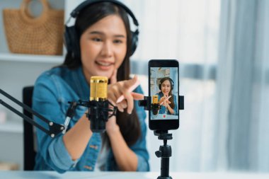 Asyalı sunucu canlı yayında canlı yayında canlı yayında sosyal medyada kulaklık takarak konuşuyor. Dinleyicileri modern stüdyoda koçluk yaparak selamlıyor. Taktik.