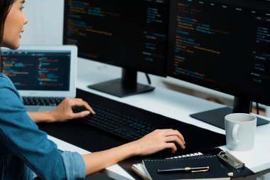 İnternet sitesi uygulamasının kodlama verileriyle birlikte online bilgi yazarak kot gömlek giyen genç Asyalı geliştirici. Güvenlik analizi ile çevrili iki ekran. Taktik.