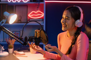 Geceleri podcast 'te olumlu konuşmalar yapan, pembe neon ışıklı modern stüdyoda sunum için dizüstü bilgisayar kullanan, gülümseyen, genç, güzel Asyalı bir etkileyiciydi. Taktik.