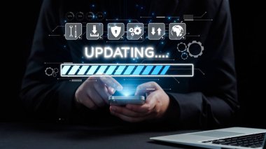 Bir kişi, modern teknolojiyi sembolize eden, güncelleme ilerleme çubuğunu gösteren dijital bir arayüzü kullanarak, karanlık bir ortamda akıllı bir telefonla etkileşime girer. Dörtgen