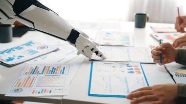 Robotik bir kol modern ofis ortamında bir iş ekibine yardım eder, veri analizi ve etkili karar verme için görsel sunumlar yoluyla işbirliğini artırır.