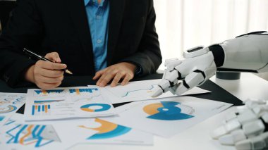 Bir iş adamı finansal verileri değerlendirirken, bir robot el de belgelere uzanarak teknoloji ve insan uzmanlığının analizlerde birleştirilmesini ön plana çıkarır.