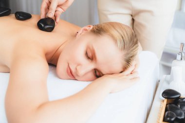 Lüks tatil köyündeki kaplıcalarda sıcak taş masajı. Gün ışığı sükunet ortamında, mutlu kadın müşteri bazalt taş masajından zevk alıyor. Rahatlatıcı bir sıcaklıkla vücudun üzerinde süzülüyor. Sessiz.