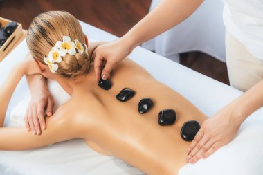 Lüks tatil köyündeki kaplıcalarda sıcak taş masajı. Gün ışığı sükunet ortamında, mutlu kadın müşteri bazalt taş masajından zevk alıyor. Rahatlatıcı bir sıcaklıkla vücudun üzerinde süzülüyor. Sessiz.