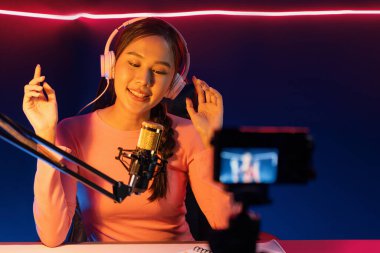 Yaratıcı yayın kanalı sosyal medyada pozitif podcasttaki dinleyicilerle birlikte müziği dinliyor, pastel renkli kulaklıklar takıyor, neon stüdyodaki kameraların mikrofon kayıtlarını kullanıyor. Taktik.