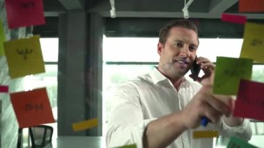 Profesyonel işadamı renkli yapışkan notlara yazılmış pazarlama stratejisi fikrine bakarken müşterilerine telefon ediyor. Proje yöneticisi duvardaki telefon analiz verileriyle konuşuyor. Yönlendirici.