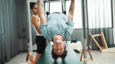 Eğitmen rehberliğinde Pilates Cadillac 'ta ters bacak yükseltme pratiği yapan sağlıklı bir müşteri. Çekirdek dayanıklılığını ve üst vücut dengesini arttırmak için Cadillac 'ı geren adam. Alışkanlık.