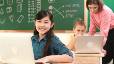 Akıllı Asyalı kız, mühendislik komut yazarken kameraya bakıyor. Çok kültürlü bir öğrenci yapay zekayı öğrenirken öğretmenler sistemi öğretiyor ya da STEM sınıfında sınıfları kontrol ediyor. Pedagoji.