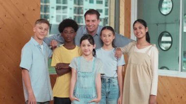 Mutlu öğretmen ve çeşitli öğrenciler kameraya gülümserken ayakta duruyorlar. Profesyonel akıllı eğitmen ve karışık ırk olan lise öğrencileri kameraya neşeli pozlar veriyor. Öğretim