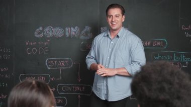 Tahtada çeşitli öğrencilere mühendislik kodları öğreten yakışıklı bir öğretmen. Mutlu çok kültürlü liseli çocuklar dizüstü bilgisayar kullanırken öğreniyor ya da programlama ya da kodlama sistemini öğreniyor. Öğretim