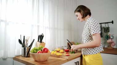 Enerjik anne, mutfak malzemeleri ile çevrili sebzeleri doğrarken modern mutfakta kahvaltı için salata yapıyor. Akıllı kadın temizlikçi yemek pişirir ve yemek hazırlar. Sağlıklı bir yaşam tarzı. Pedagoji.