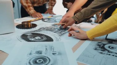 Bir grup mühendis bir çalışma istasyonunun etrafında toplanarak planlar üzerinde gösterilen karmaşık mekanik tasarımları, yaratıcı bir çalışma alanında takım çalışması ve yenilikleri tartıştılar. SACTR