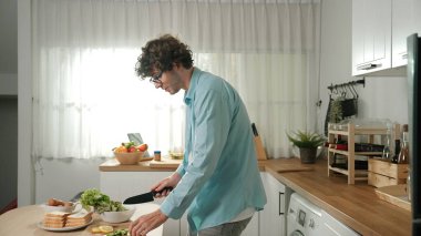 Mutlu baba yemek pişirirken müziğe geçiyor ve modern mutfakta öğle yemeği hazırlıyor. Aktif baba, sebze ve mutfak gereçleri ile çevrili sağlıklı yemek ya da salata yaparken şarkıyla dans ediyor. Pedagoji.