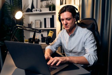Sunucu kanalı akıllı yayıncı laptopta canlı sosyal medya uygulaması arıyor, kulaklık takıyor ve modern ofis stüdyosundaki mikrofonu kullanıyor. Bireysel.