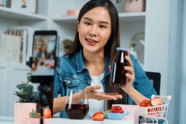 Gülümseyen, güzel Asyalı genç, lezzetli karışık çilek ve kiraz suyu detoksu içeceklerini inceleyen, sosyal medyada özel promosyon satışı için sağlıklı ürünler sergileyen. Taktik.