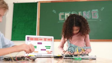 Dizüstü bilgisayar ekranında çalışan çeşitli öğrenci kodlama mühendisliği komut yazılımı ve yapay zeka programlaması yapıyor. Amerikalı kız, erkek makine tamir ederken ekipmanları teftiş ediyor. Pedagoji.