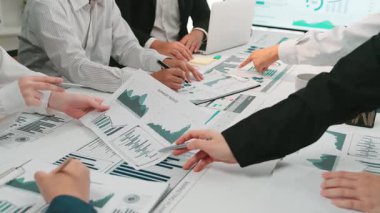 Bir grup profesyonel, çizelge ve raporlarla çevrili bir iş toplantısı sırasında tartışıyorlar. Stratejik kararları yönlendirmek için veri analizinde işbirliği yapıyorlar. SACTR