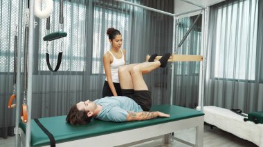 Cadillac ekipmanları üzerinde bacak kaldırma egzersizinde müşteriye yardımcı olan yetenekli pilates eğitmeni. Kadın antrenör, Cadillac 'ın bacak gerdirme hareketine yardım ediyor. Temel bağlantıyı geliştirmek için, bacak esnekliği için. Alışkanlık.