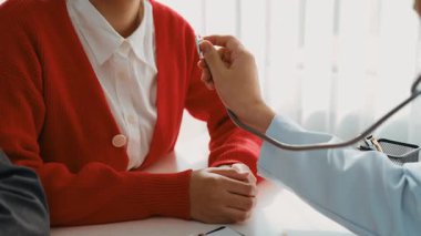 Hasta klinikte ya da hastane ofisinde doktor randevusuna gidiyor. Hastaların nabzını steteskopla kontrol edip risk faktörünü belirleyen doktor semptomları inceliyor. Panorama. Katı.