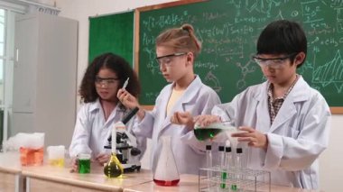 Çocuklar laboratuvarda karatahta başında dururken fen dersinde deney yapıyorlar. Mutlu öğrenci biyokimyasal sıvıyı keşfederken ve incelerken ve karıştırırken. Pedagoji.