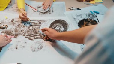 Bir grup profesyonel, planlar ve araçlarla çevrili, mühendislik tasarımında takım çalışması ve yenilik sergileyen parlak bir çalışma alanında motor mekaniği üzerinde işbirliği yapıyor. SACTR