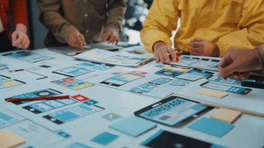 Çeşitli bir ekip kullanıcı arayüzü tasarımları üzerine etkileşimli beyin fırtınası yapıyor, renkli prototipler ve etkin planlama için masadaki yapışkan notlar kullanılıyor. SACTR