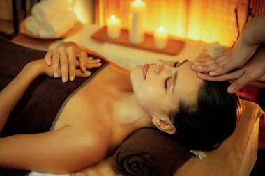 Beyaz kadın stres önleyici kafa masajı yapmaktan ve lüks otel veya otelde sıcak mum ışığında yüz güzelliği eğlencesi yapmaktan zevk alıyor. Sessiz.