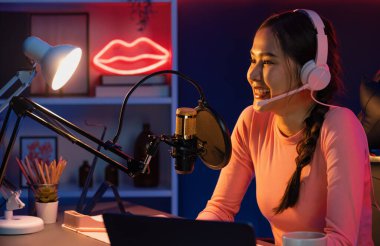 Geceleri podcast 'te olumlu konuşmalar yapan, pembe neon ışıklı modern stüdyoda sunum için dizüstü bilgisayar kullanan, gülümseyen, genç, güzel Asyalı bir etkileyiciydi. Taktik.