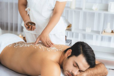 Lüks spa salonunda sıcak mum ışığı atmosferi olan lüks kaplıcalarda deri dökme tedavisi gören mutlu bir adam. Sağlık kaplıcasında güzellik tedavisiyle tuz temizliği. Sessiz.