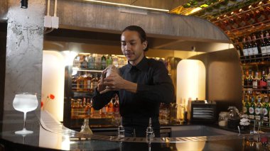 Asyalı akıllı barmen karışık kokteyl sallayarak lüks tezgah hazırlıklarına hazırlanıyor, kameranın önüne bakarak özel bir içecek hazırlıyor. Özel gece hayatı lüksü. Vinosity.